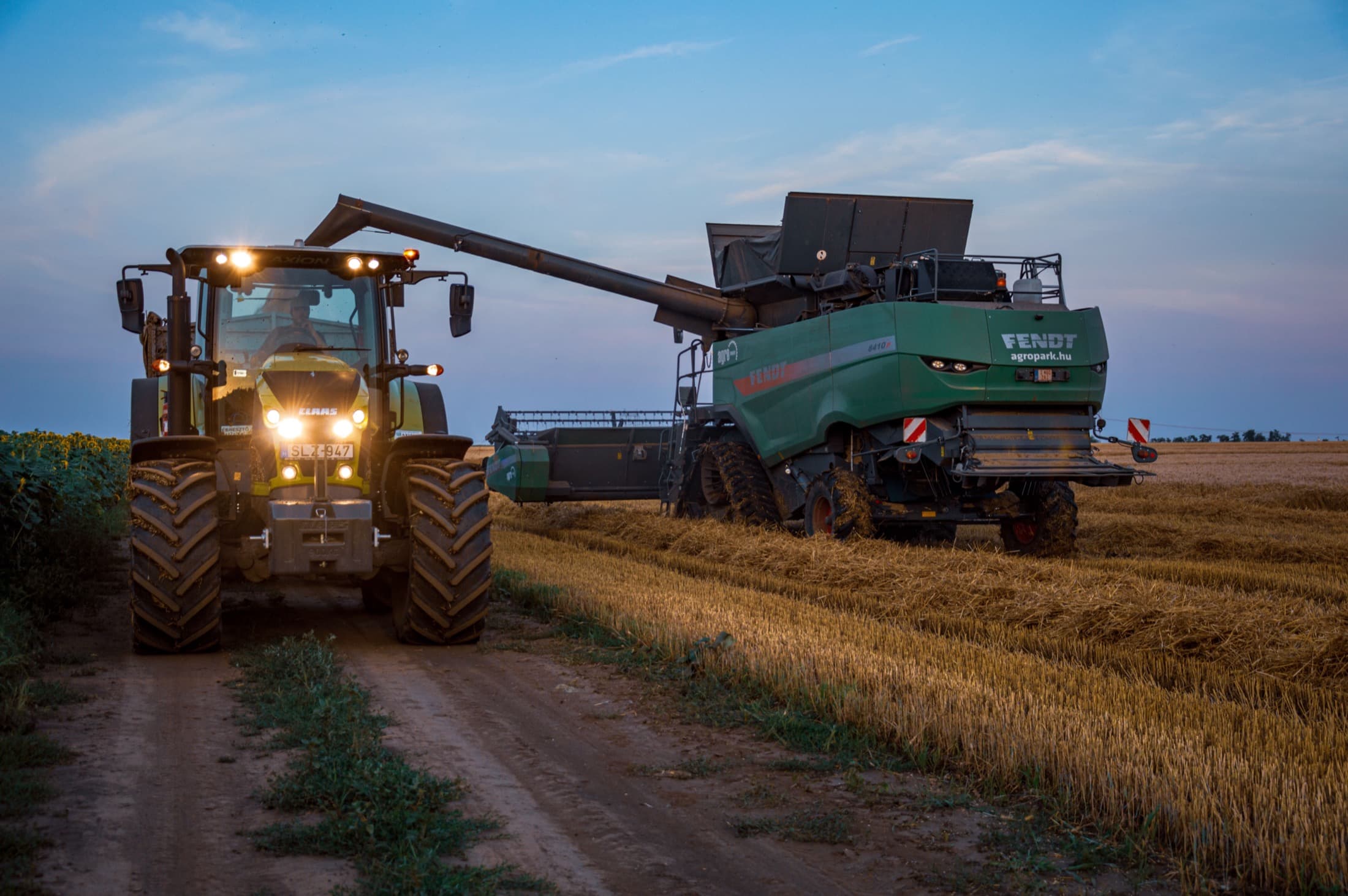 Une moissonneuse et un tracteur au travail, au crépuscule