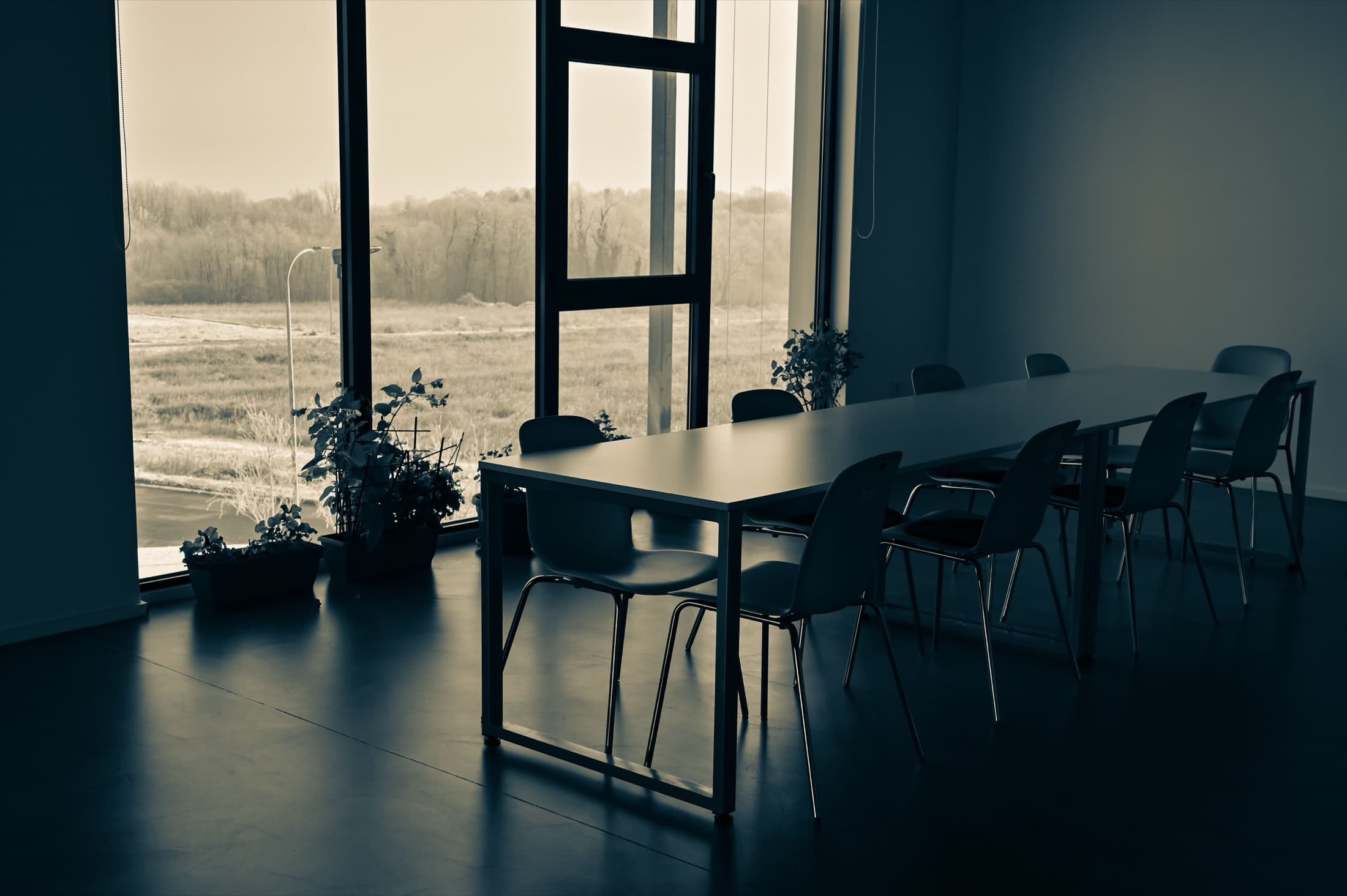 Une longue table de réunion inoccupée, devant une baie vitrée