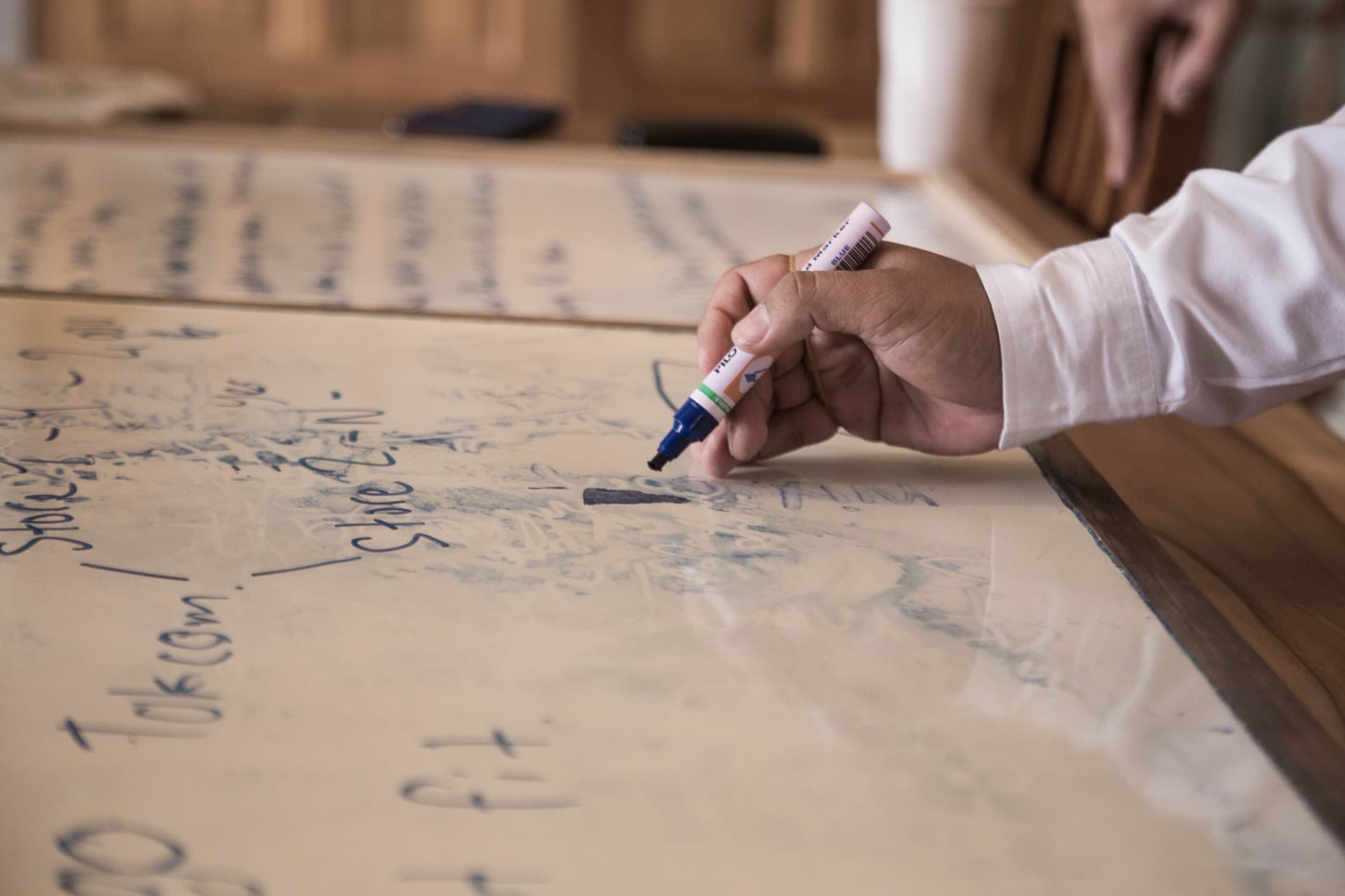 Une main écrit au feutre sur un tableau blanc déjà couvert de notes