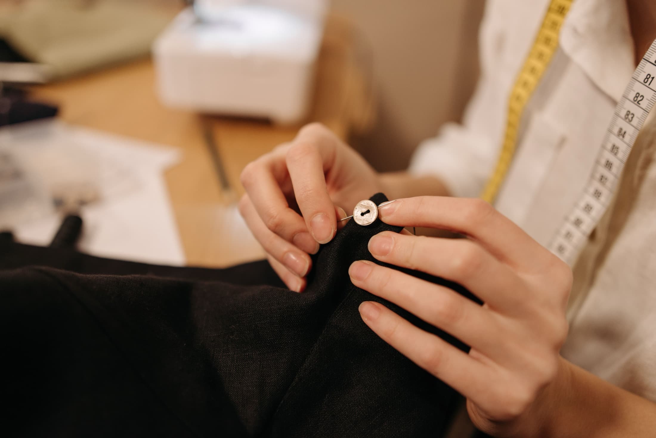 Une couturière fixe un bouton sur un vêtement, en atelier