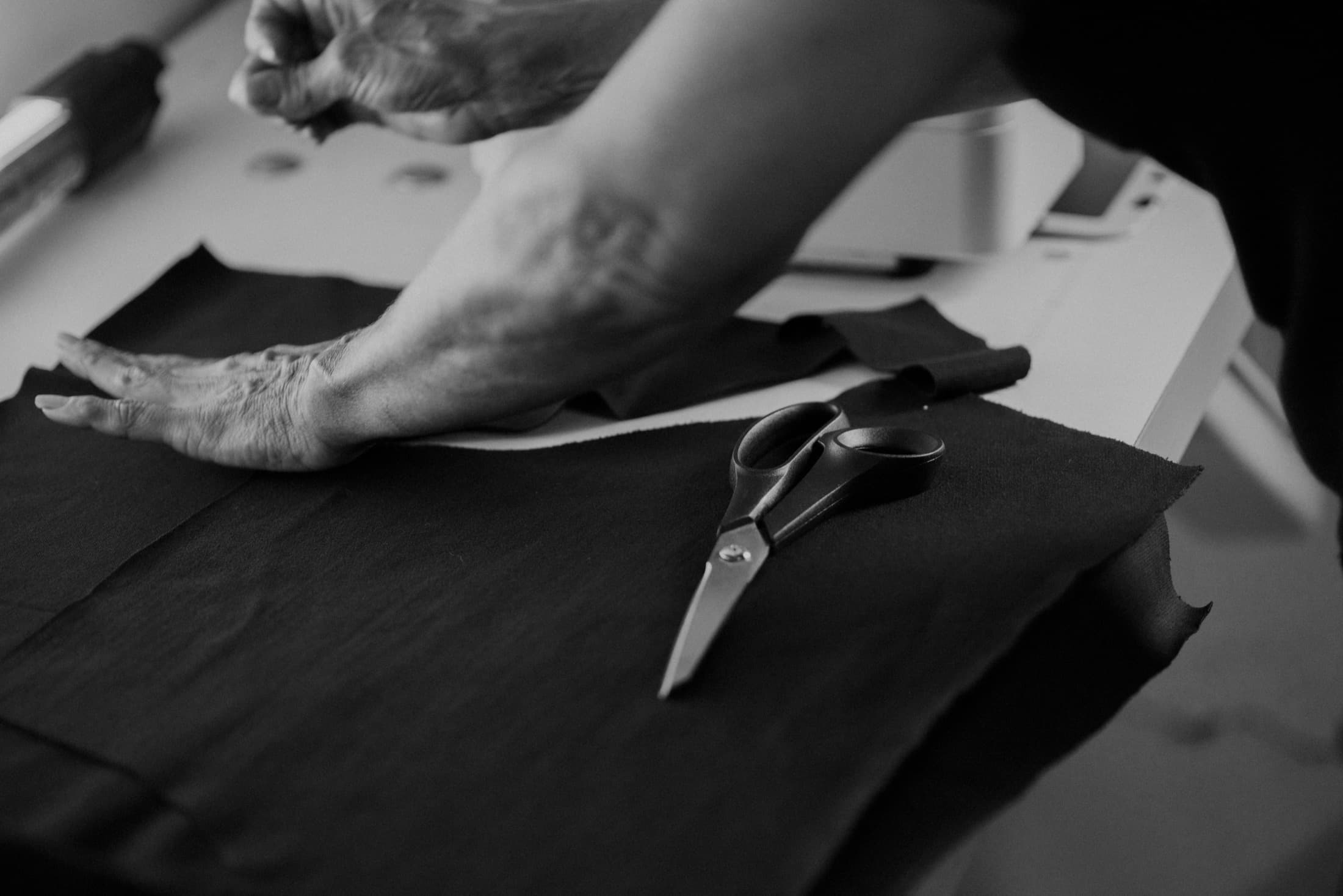 Les mains d'un coupeur sur une pièce de tissu noir, ciseaux posés