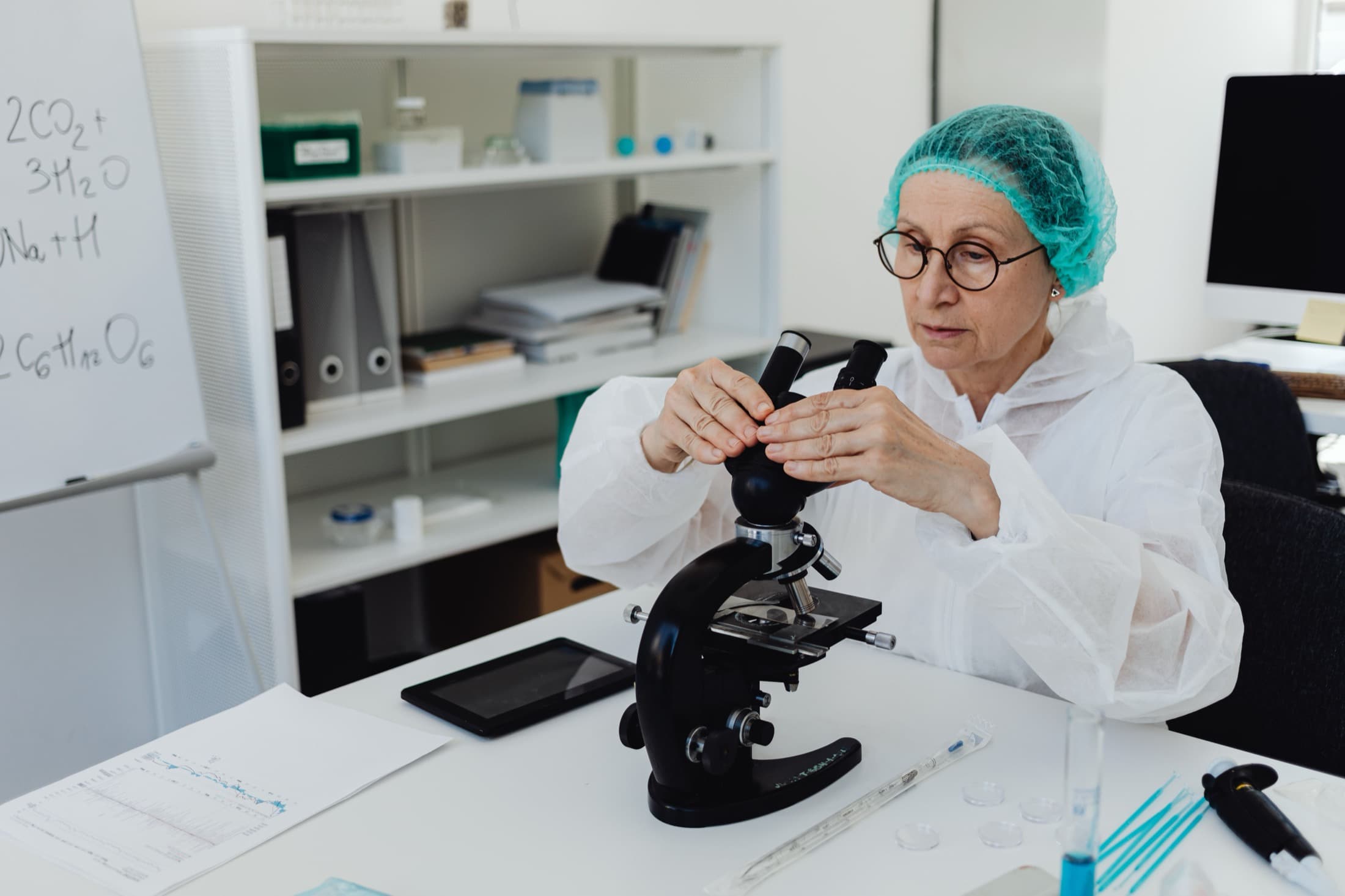 Une chercheuse règle son microscope, en blouse