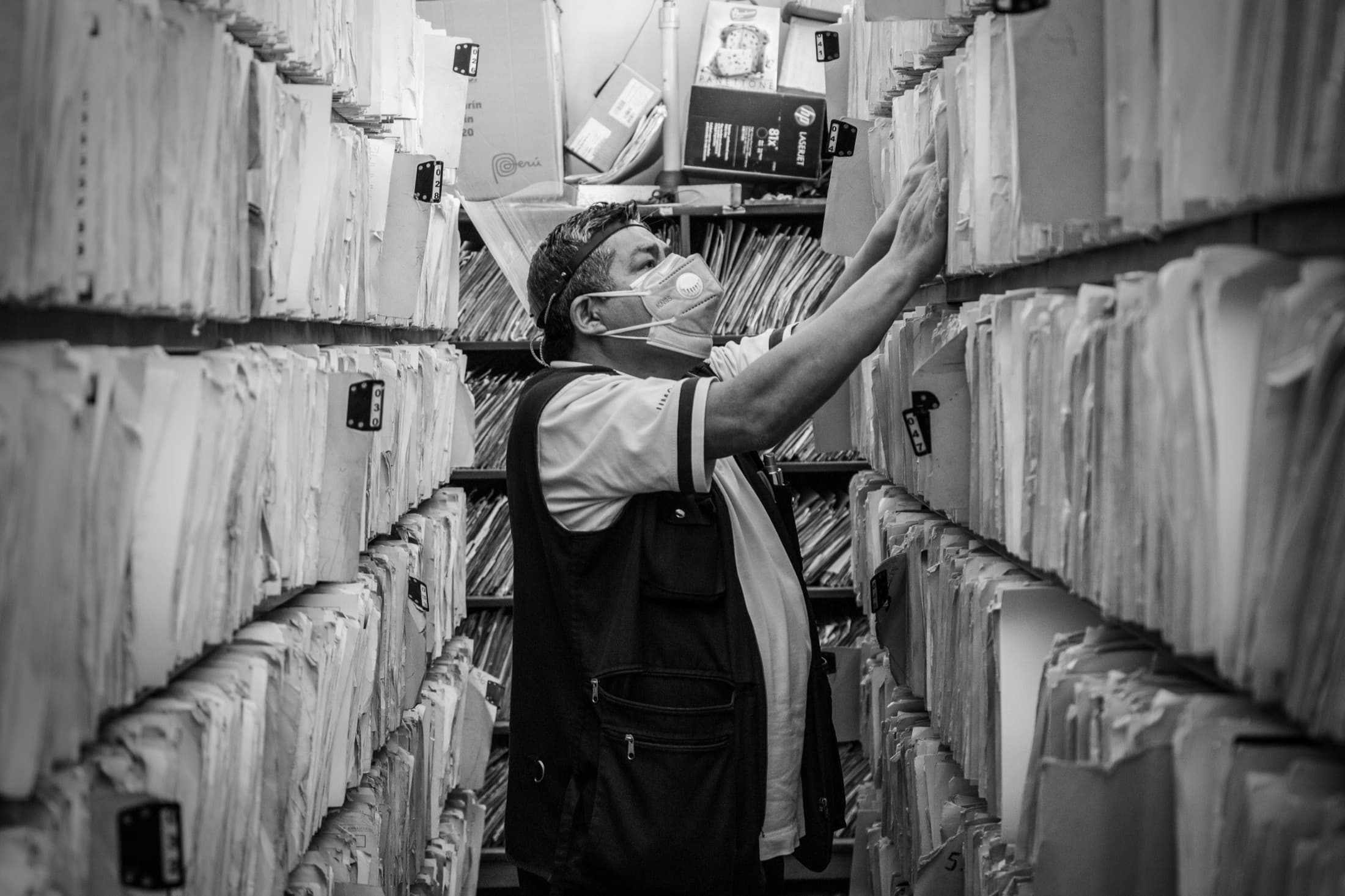 Une archiviste cherche un dossier dans des rayonnages saturés