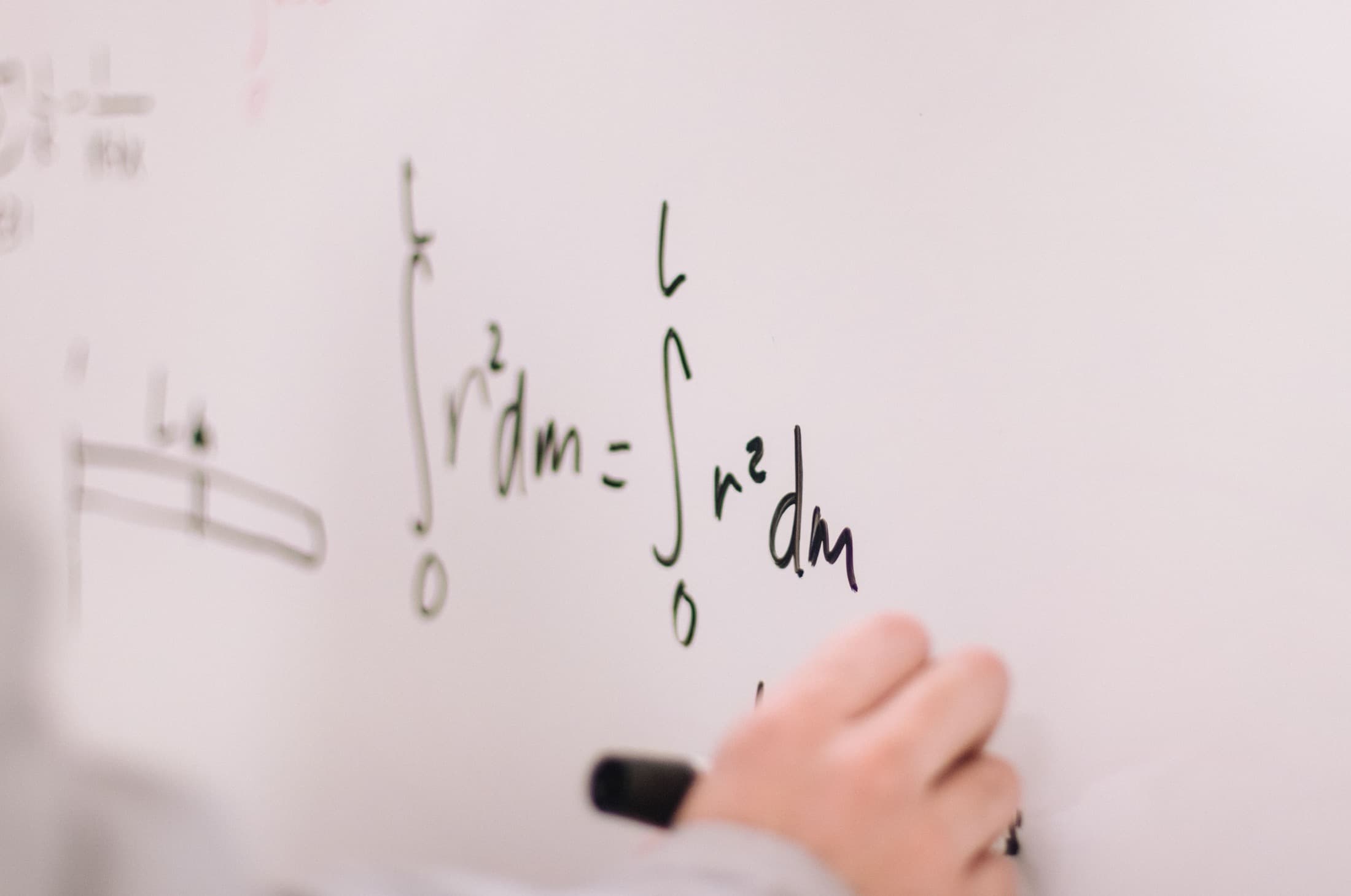 Une main écrit une formule au feutre sur un tableau blanc