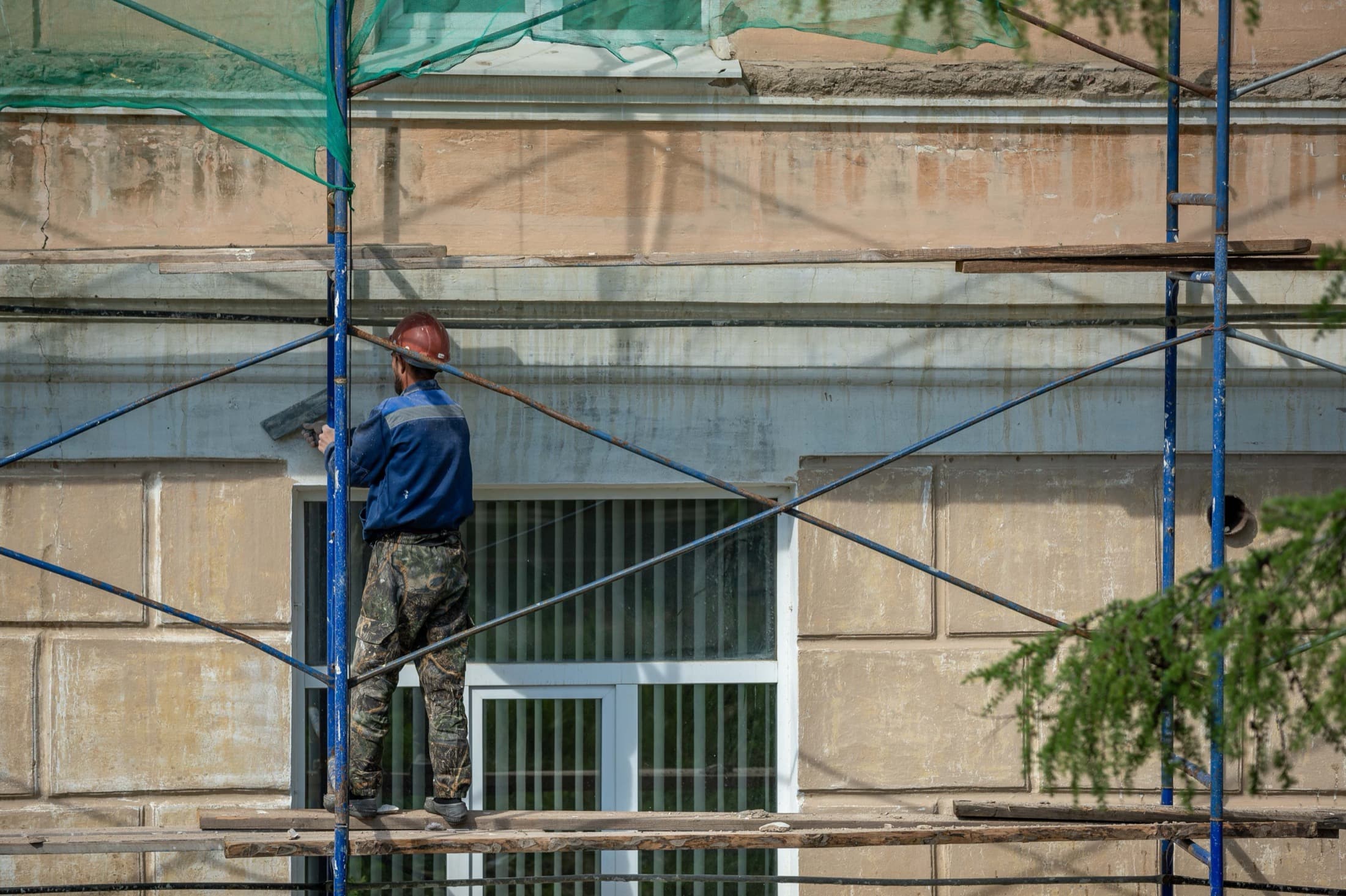 Un ouvrier travaille sur un échafaudage, en ravalement de façade